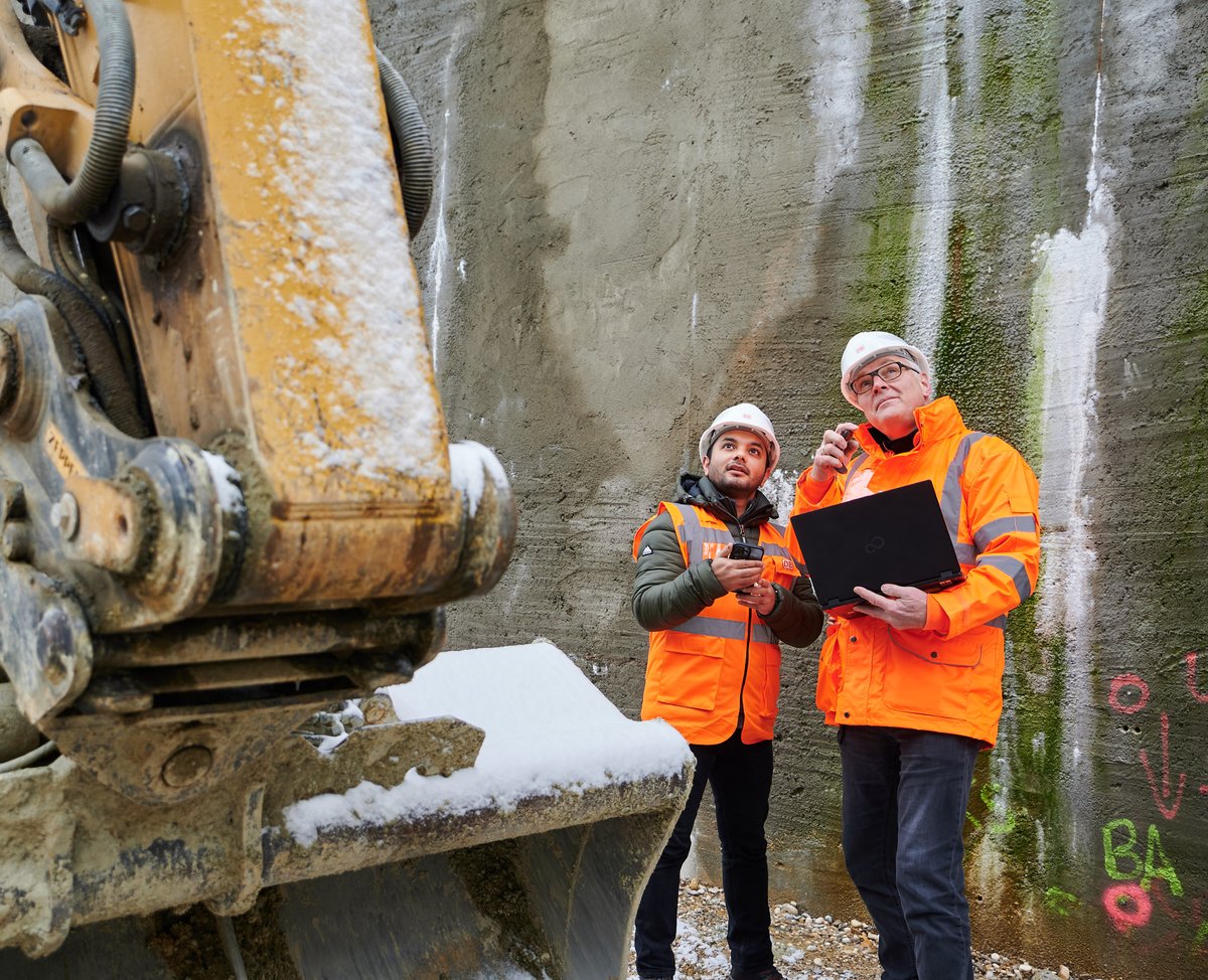 Sahil Sharma with a colleague on a rail infrastructure construction site, reviewing BIM data on a laptop